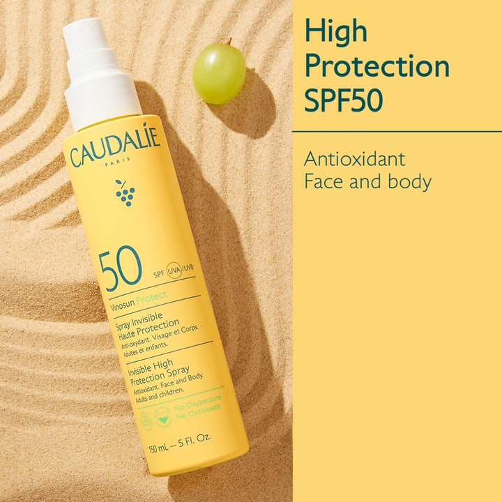 Caudalie Vinosun High Protection Spray SPF50 150 ml solkrem i gul sprayflaske på sand med en grønn drue
