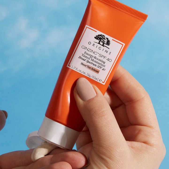 Origins GinZing SPF 40 50 ml farget dagkrem trykkes ut av en oransje tube og viser en kremet tekstur.