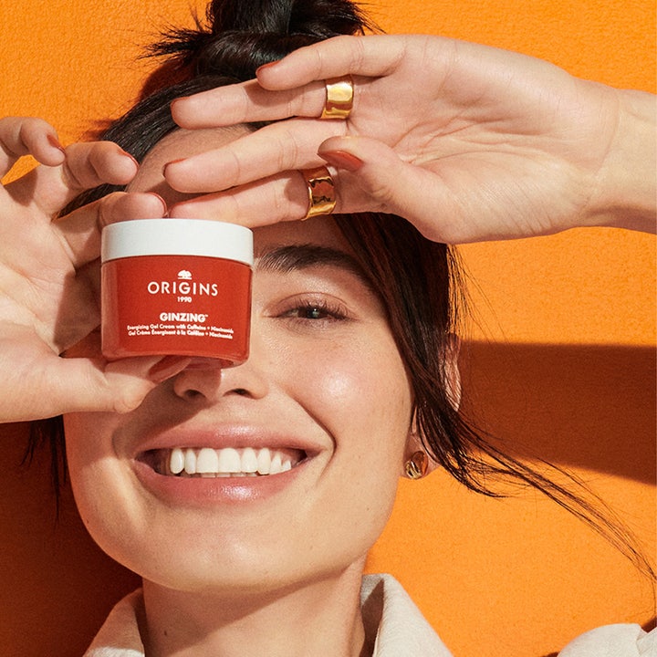 Origins Ginzing Energizing Gel Face Cream 30 ml energigivende dagkrem holdt av en smilende kvinne i sollys.