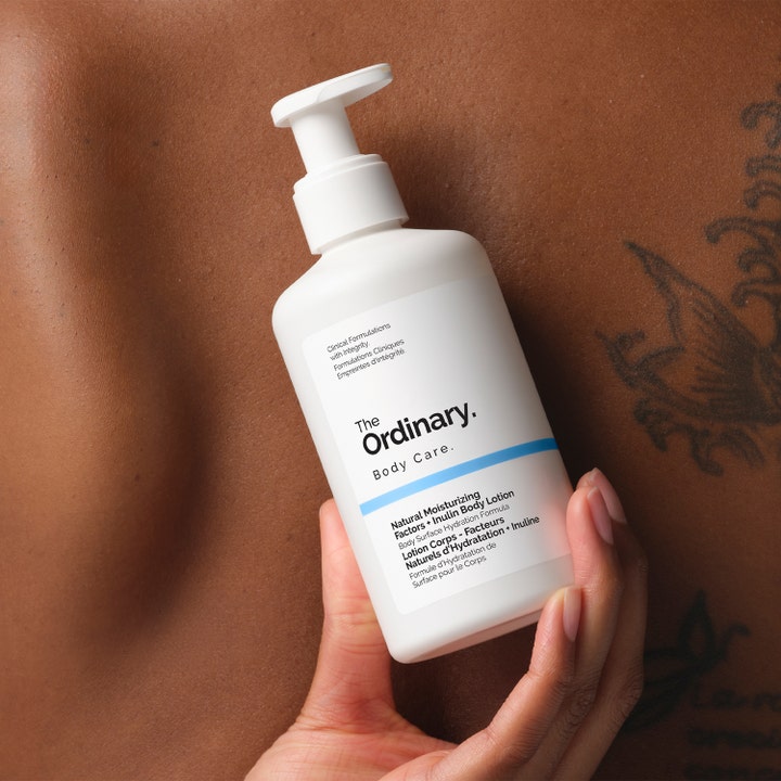The Ordinary NMF + Inulin Body Lotion 240 ml fuktighetsgivende hudpleie i hvit pumpeflaske holdt mot hud