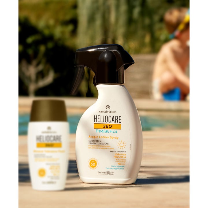 Heliocare Pediatrics Atopic Lotion Spray 250 ml gir SPF 50 beskyttelse i hvit sprayflaske utendørs ved bassenget.