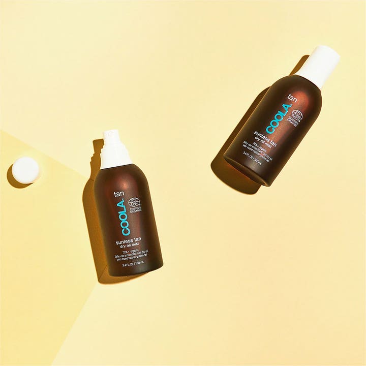 COOLA Sunless Tan Dry Oil Mist 100 ml selvbruning gir naturlig glød vist med to brune sprayflasker på gul flate.