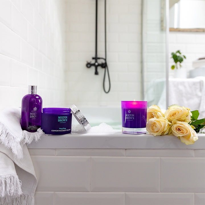 Molton Brown Relaxing Ylang Ylang Bath & Shower Gel 300 ml beroligende dusjsåpe i lilla flaske ved hvite roser