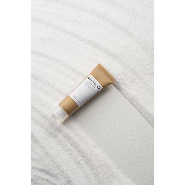 SKIN1004 Madagascar Centella Ampoule Foam 125 ml ansiktsrens i lysebrun tube plassert på hvit sand med vanndråper.