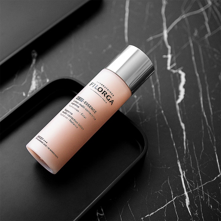 Filorga NCEF-Essence 150 ml fuktighetsgivende essence i frostet rosa flaske med sølvkork på svart marmor