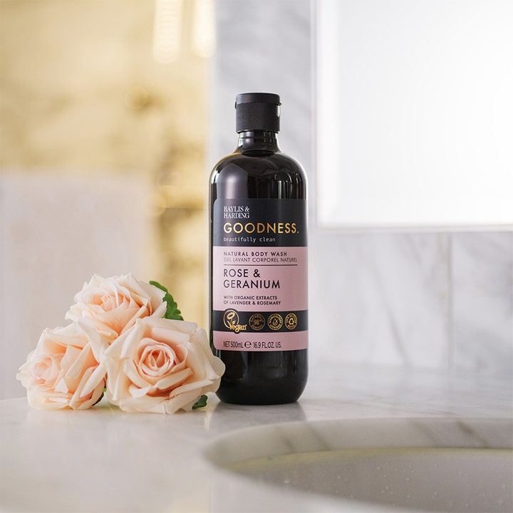 Baylis & Harding Goodness Body Wash Rose & Geranium 500 ml vegansk dusjsåpe i mørk flaske ved ferskenfargede roser.