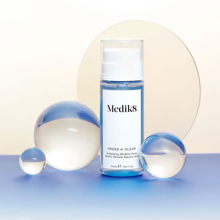Medik8 Press & Clear 150 ml eksfolierende toner med BHA i blå pumpeflaske omgitt av dekorative glasskuler