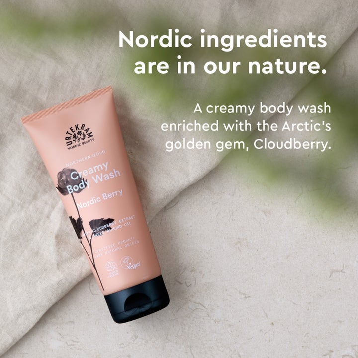 Urtekram Nordic Berry Creamy Body Wash 200 ml pleiende dusjsåpe i ferskenfarget tube på lyst tekstilunderlag.